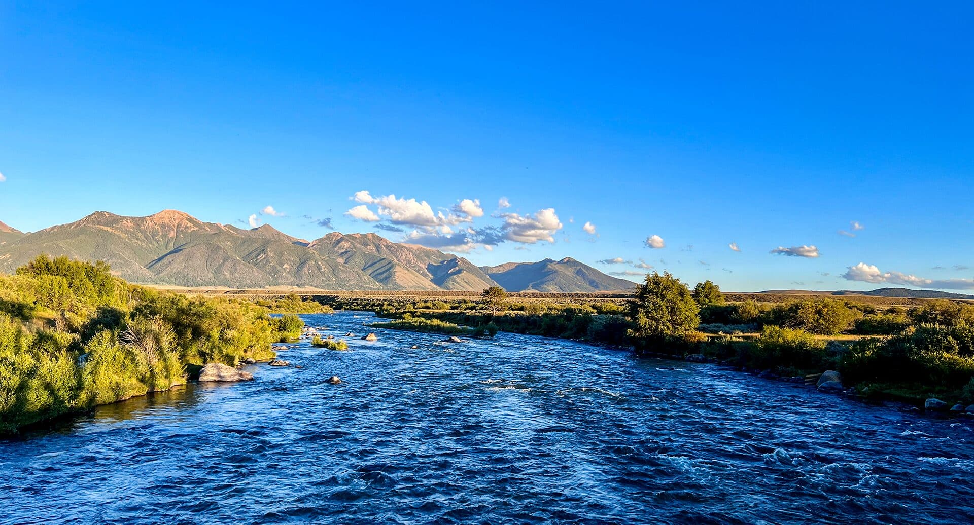 The Madison River in Montana with the Madison Range rising in the distance under a blue sky